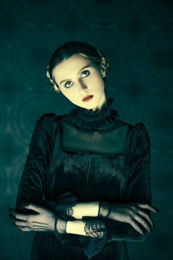Makyaj ve saç stili. Gotik roman, mistisizm. Siyah kadife elbiseli ve dantel eldivenli dramatik esmer bir kızın portresi, gecenin karanlığında eskimiş bir arka planda duruyor..