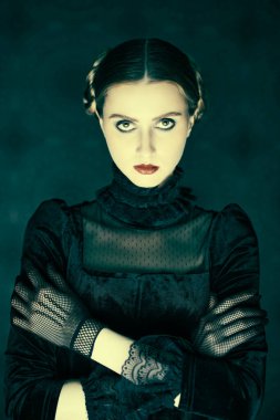 Gotik roman, mistisizm. Şık siyah kadife elbise ve dantel eldiven giymiş esmer bir kızın portresi, gecenin karanlığında eskimiş bir arka planda duruyor. Makyaj ve saç stili.