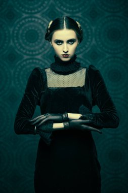 Şık siyah kadife elbise ve dantel eldiven giymiş esmer bir kızın portresi, gecenin karanlığında eskimiş bir arka planda duruyor. Makyaj ve saç stili. Gotik roman, mistisizm..