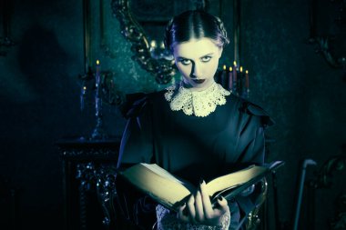 Addams Ailesi romanı. Beyaz yakalı, düzgün siyah elbiseli esmer bir kız gecenin karanlığında kasvetli gotik bir kalede duruyor ve antik bir kitap okuyor. Mistik roman, gotik.