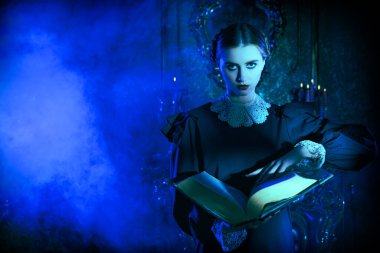 Addams Ailesi romanı. Siyah elbiseli esmer, ciddi bir kız gecenin karanlığında kasvetli bir gotik kalede duruyor ve antik bir kitap okuyor. Mistik roman, gotik. Boşluğu kopyala.