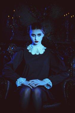 Mistik gotik roman, korku. Kasvetli bir kalede, koltukta oturan, katı siyah elbiseli, beyaz yakalı, tuhaf, esmer bir kızın portresi. Addams Aile Stili. 