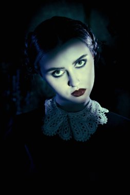 Beyaz yakalı, düzgün siyah elbiseli esmer bir kız kasvetli gotik bir kalede duruyor ve kameraya pek dostça görünmüyor. Addams Ailesi. Gotik kara komedi. Boşluğu kopyala.