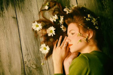 Bahar ve yaz havası. Dalgalı saçlı, tahta bir zeminde uzanmış, saçlarında beyaz çiçeklerle güzel bir kız. Doğal kozmetikler. Kadın güzelliği ve moda. Boşluğu kopyala. 