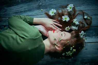 Bahar ve yaz havası. Dalgalı saçlı, tahta bir zeminde uzanmış, saçlarında beyaz çiçeklerle güzel bir kız. Doğal kozmetikler. Kadın güzelliği ve moda.