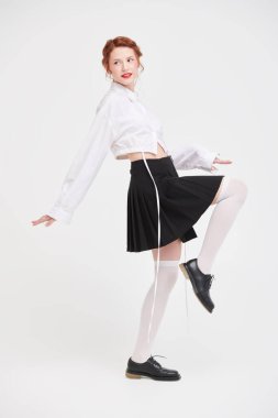 Bahar ve yaz modası. Beyaz gömlekli ve siyah etekli beyaz bir duvara karşı poz veren kızıl saçlı güzel bir kızın tam boy fotoğrafı.. 