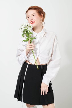 Kıvırcık kızıl saçlı güzel bir kız ve beyaz arka planda bir çiçek dalıyla beyaz bir bluz içinde hoş, ferahlatıcı bir makyaj pozu. Bahar ve yaz havası. Kadın güzelliği ve moda.