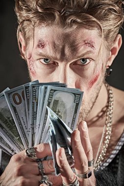 Suç dünyası, paranın gücü. Parmaklarında yüzükler olan zengin, zalim bir adam parayı tutuyor ve şeytani bir bakışla kameraya bakıyor.. 