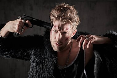 Yüzünde morluklar ve yaralar olan, beton duvarlı karanlık bir odada elinde silahla duran sert bir erkek haydut vuruldu. Aksiyon filmi kahramanı. Kötü adam konsepti. 