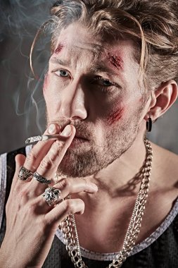 Aksiyon filmi kahramanı. Yüzünde morluklar ve yaralar olan, beton duvarlı karanlık bir odada sigara içen sert bir erkek haydutun fotoğrafı. Kötü adam konsepti. 