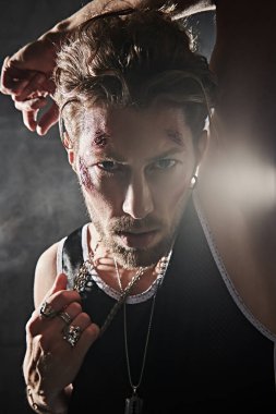 Yüzünde morluklar ve yaralar olan sert bir erkek haydut, karanlık bir odada duruyor ve agresif bir şekilde bakıyor. Kötü adam konsepti. Aksiyon filmi kahramanı.