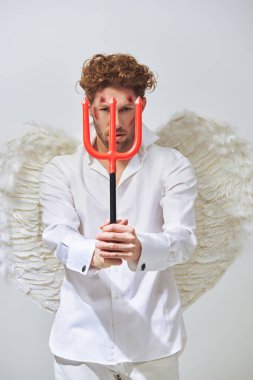 Seksi yakışıklı bir adam, Düşmüş Melek Lucifer yüzünde yaralar olan, kameraya baştan çıkarıcı bir şekilde bakan bir mızrak tutuyor. Sevgililer Günü. Fantezi. Stüdyo beyaz arkaplan.