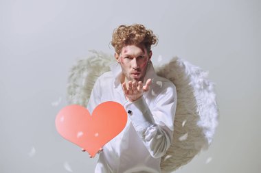 Cesur yakışıklı adam aşk tanrısı yüzünde yaralar olan aşk tanrısı ellerinde kırmızı bir kalp tutuyor. Sevgililer Günü. Boşluğu kopyala.