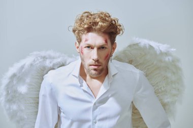 Beyaz elbiseli, beyaz kanatlı, yüzünde yaraları olan çekici bir aşk meleği kameraya bakıyor. Aşk Tanrısı Aşk Tanrısı. Sevgililer Günü. Fantezi kahramanı aşık..