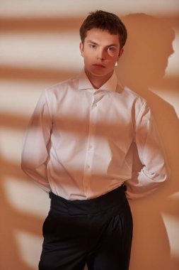 Beyaz gömlekli, siyah pantolonlu, beyaz ve turuncu renkli stüdyo ışıklarıyla poz veren yakışıklı bir gencin sanat portresi. Işık ve gölge. Erkek Moda ve Güzellik. 