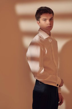 Erkek Moda ve Güzellik. Beyaz gömlekli, siyah pantolonlu, beyaz ve turuncu renkli stüdyo ışıklarıyla poz veren yakışıklı bir gencin sanat portresi. Işık ve gölge.