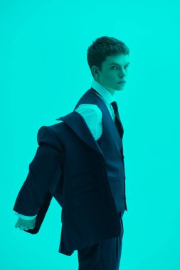 Klasik beyaz gömlekli, kol düğmeli ve zarif takım elbiseli yakışıklı, bakımlı genç bir adam. Stüdyonun arka planında akuamarin ışıklandırmalı. Erkek modası ve güzelliği. Klasik biçim.