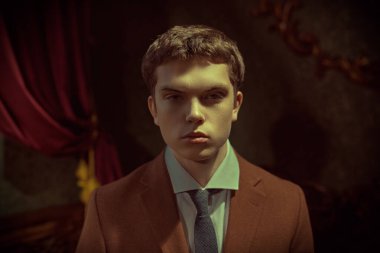 Pahalı takım elbiseli saygıdeğer bir genç adam zengin bir dairede klasik bir iç mimarisi ile duruyor. Erkek modası, lüks tarzı..