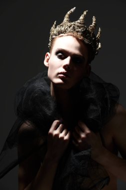 Resim çekimi. Siyah dumanlı gözleri olan, çıplak vücutla poz veren ve siyah stüdyo arka planında tacı olan şehvetli yakışıklı bir genç. Erkek güzellik konsepti. Yüksek moda.