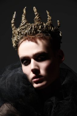 Siyah dumanlı gözleriyle çıplak vücut ve siyah bir arka planda taçla poz veren şehvetli yakışıklı bir gencin sanat portresi. Erkek güzellik konsepti. Yüksek moda.