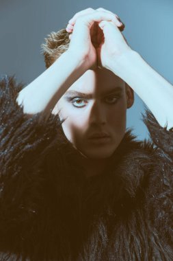 Makyaj, saç stili, makyaj malzemeleri. Kısa saç kesimi ve siyah dumanlı gözleriyle stüdyoda siyah kürklü poz veren şık bir gencin portresi. Moda ve erkek güzelliği. 