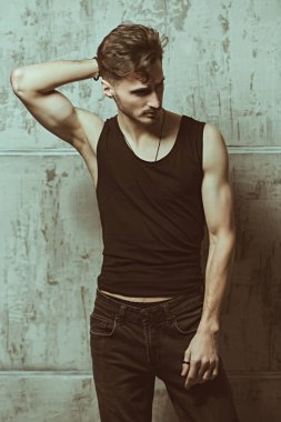 Erkeklik. Moda ve erkek güzelliği. Siyah bir bluz ve beton bir duvara karşı kot giymiş yakışıklı, esmer bir adamın portresi.. 