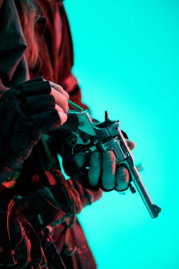 Bir adamın elindeki tabancaya yakından ateş edilmiş. Kıyametten sonraki dönem. Hayatta kalmak için silah. Açık mavi arkaplan.