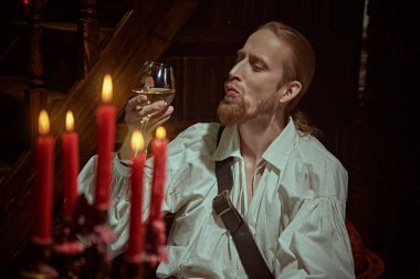 Beyaz gömlekli bir silahşör elinde bir bardak şarapla kalesinde dinleniyor. 16.-17. yüzyılın tarihi yeniden yapılandırması.