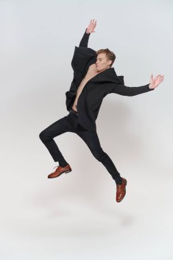 Sevinçten zıplayıp eğlenen yakışıklı, neşeli bir genç. Beyaz arka planda stüdyo boy portresi. Mutlu insanlar, duygular. 