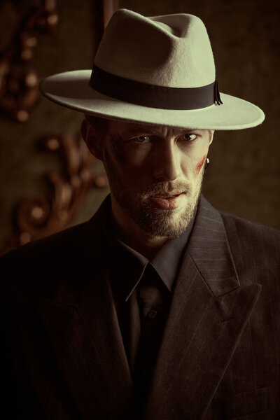 A tough gangster man in an elegant black suit and a white hat in a luxury apartment. Retro style. The criminal world of the mafia. Detective movie. Copy space.