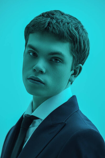 Мужская мода и красота. Красивый ухоженный молодой человек, позирующий в классической белой рубашке и элегантном костюме на фоне студии с аквамариновым освещением. Классический стиль.