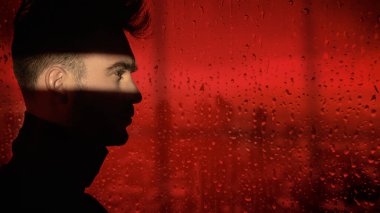 Karanlık arka planda gölgede duran bir adamın profil portresi. Yüzü bir kırmızı ışık demeti tarafından aydınlatılır. Uzayı kopyala Psikolojik sanat portresi.