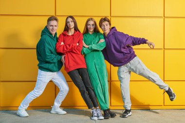 Parlak gençlik modası. Modern gençlik kıyafetleri içinde dört aktif genç açık sarı bir binanın yanında sokak balesi yapıyor ve birlikte eğleniyorlar. Modern gençler..