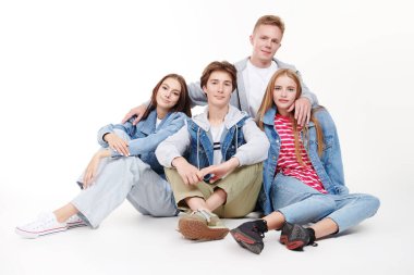 Beyaz bir stüdyo arka planında oturan dört neşeli ve gülümseyen kotlu gencin stüdyo fotoğrafı. Denim tarzı, gençlik tarzı..