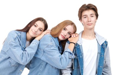 İki güzel genç kız ve şık kotlar giymiş yakışıklı bir gencin beyaz stüdyo arka planında poz verdiği bir moda çekimi. Denim tarzı, gençlik tarzı. Eğitim. 