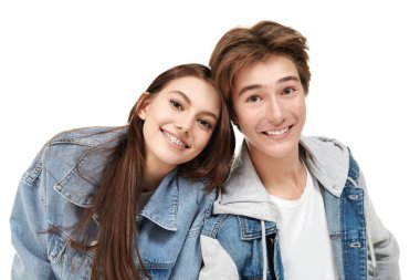 Beyaz arka planda poz veren şık kot elbiseli, gülümseyen genç erkek ve kız portresi. Denim tarzı, gençlik tarzı..
