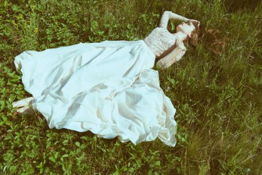 Muhteşem dantel bir elbise giymiş güzel bir kız doğadaki yeşil çimlerin üzerinde uzanıyor. Yaz güzelliği ve moda. 