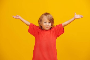 Parlak kırmızı tişörtlü, sarı saçlı, şirin bir çocuğun stüdyo fotoğrafı. Sarı arka plan. Çocuklar ve duygular. Boşluğu kopyala.