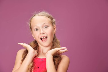 Kırmızı elbiseli, saçları örgülü komik sarışın bir kız komik bir yüz ve sürpriz yapar. Çocukların duyguları ve oyunları. Kopyalama alanı olan mor arkaplan. 