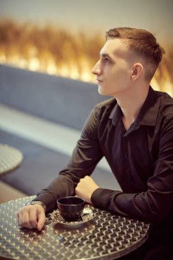 Yakışıklı genç adam rahat bir kafede bir masada oturup bir fincan kahve içiyor. İnsanlar ve yaşam tarzı. 