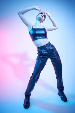 Moda ve rock tarzı. Siyah deri kıyafetler ve siyah botlarla poz veren bir mankenin tam boy portresi. Işık stüdyosu arka planında karışık ışıklandırma.