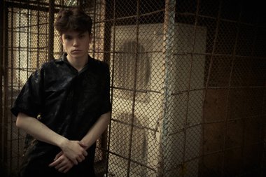 Şehir yaşam tarzı. Siyah elbiseli modern bir genç büyük bir şehrin karanlık bir sokaktaki metal bir ızgaraya yaslanmış duruyor. Boşluğu kopyala.