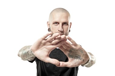 Gayri resmi görünümlü, kafası kazınmış, dudakları ve kulaklarında piercingler olan vücudunda dövmesi olan bir adam avuç içlerini kameraya uzatıyor. Beyaz stüdyo geçmişi.