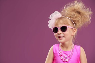 Parlak mücevherleri, pembe güneş gözlükleri ve modaya uygun saç stiliyle kıpkırmızı giyinmiş güzel bir moda kızının portresi. Stüdyo fuşya arka planı ve fotokopi alanı. Tatil.