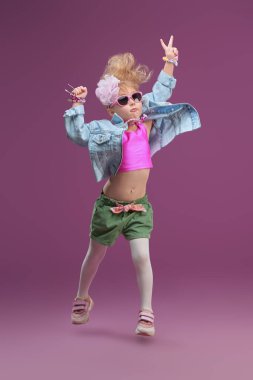 Çocuk modası. Parlak elbiseli, mücevherli ve 80 'ler tarzında havalı bir saç stili olan güzel bir moda kızı portresi. Stüdyo mor arka plan. Çocuk pop ve rock yıldızı.
