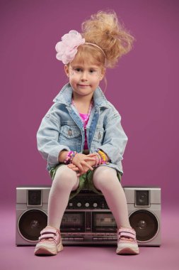 80 'lerin tarzında güzel bir şarkıcı kız teybe oturur ve gülümser. Çocuk pop ve rock şarkıcısı. Fuşya arka planında stüdyo portresi.