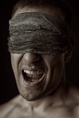 Çıplak gövdeli bir adamın yakın plan portresi. Gözlerinde sargı beziyle durup çığlık atan bir adam. Siyah arka plan. Psikolojik resim.