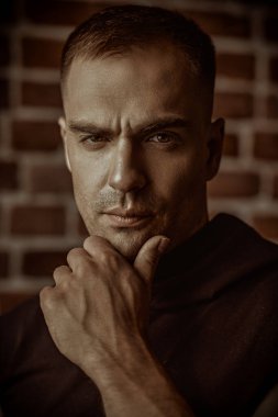 Siyah kapüşonlu güçlü bir adamın yakın plan portresi, odaklanmış ve yoğun bir şekilde kameraya bakıyor. Arka planda tuğla duvar var. Halk konsepti. Erkekler, erkeklik ve güç..