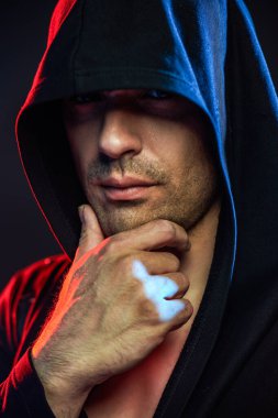 Güçlü, kendine güveni olan atletik yapılı bir adam kaputun içinde kameraya güvenle bakıyor. Stüdyo portresi ve karışık ışık. Güç sporları. Boksör. Savaşçı..