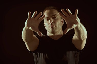 Güçlü, kaslı bir adam kameraya bakar ve ellerini ileri uzatır. Karanlık bir arkaplanda, metin için yeri olan stüdyo portresi. İnsanlar ve duygular. Yaşam tarzı, seçimler. Spor..